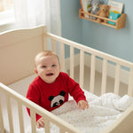 Baby in a red sweater with a panda design sitting in a crib.
