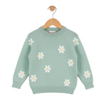 Green sweater with white daisy patterns on a wooden hanger against a white background