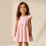 Young girl wearing a pink dress with a bow on a neutral background