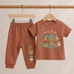 Children's brown outfit with 'born to be awesome' shirt and pants on hangers against a beige background