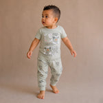 Child wearing a light green pajama set with animal prints on a beige background