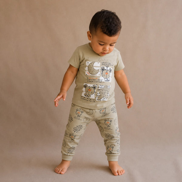 Child wearing a green t-shirt and matching pants with animal prints on a beige background