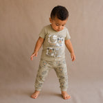 Child wearing a green t-shirt and matching pants with animal prints on a beige background