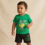 Child wearing a green t-shirt with a dinosaur graphic and black shorts on a beige background