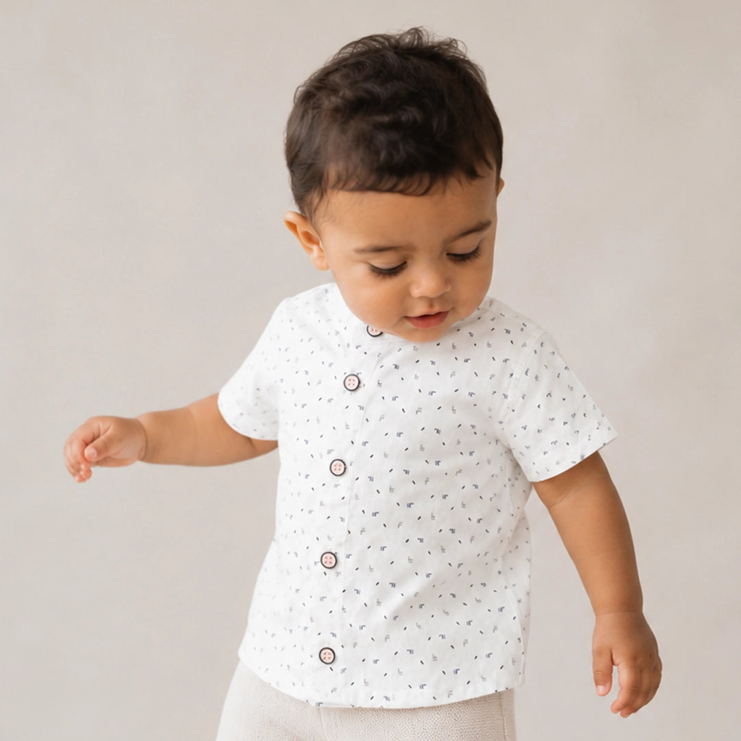 Baby wearing a white shirt with black patterns on a plain background