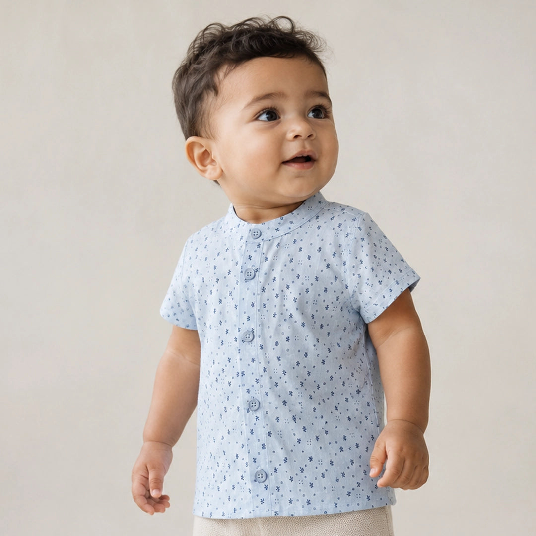 Child wearing a light blue shirt with small patterns and dark jeans on a plain background