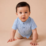 Child wearing a light blue shirt with small patterns and dark jeans on a plain background