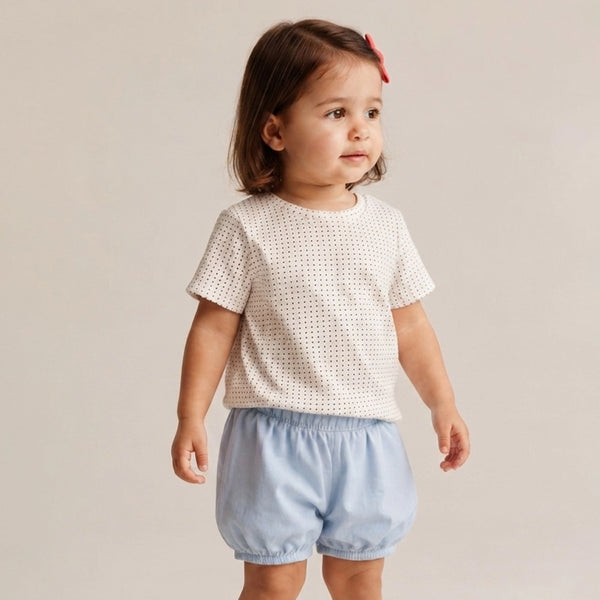 Child wearing a white patterned top and light blue shorts on a plain background