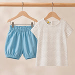 Children's outfit with blue shorts and patterned shirt on hangers against a beige background