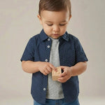 Child wearing a blue polka dot shirt holding a wooden block with a letter on it.