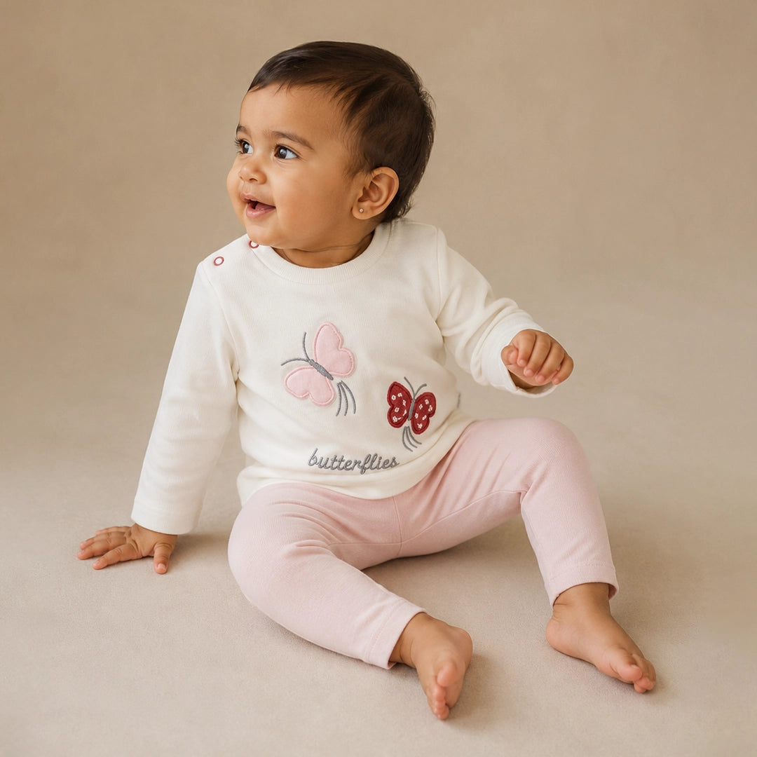 Child wearing a white sweater with butterfly designs and pink pants on a neutral background
