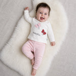 Child wearing a white sweater with butterfly designs and pink pants on a neutral background