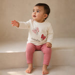 Child wearing a white shirt with butterfly designs and pink pants on a neutral background