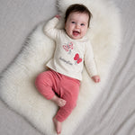 Child wearing a white shirt with butterfly designs and pink pants on a neutral background