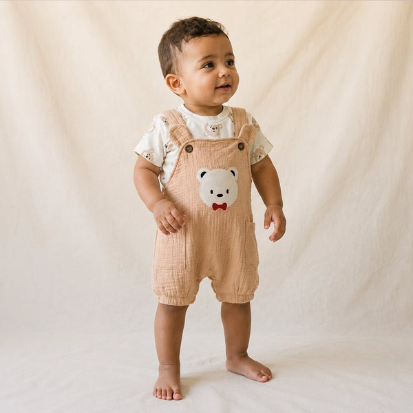 Baby wearing a beige romper with a bear face design on a plain background