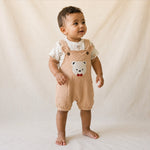 Baby wearing a beige romper with a bear face design on a plain background