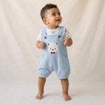 Baby wearing a light blue romper with a bear design on a neutral background