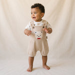 Baby wearing a beige romper with a bear design on a plain background