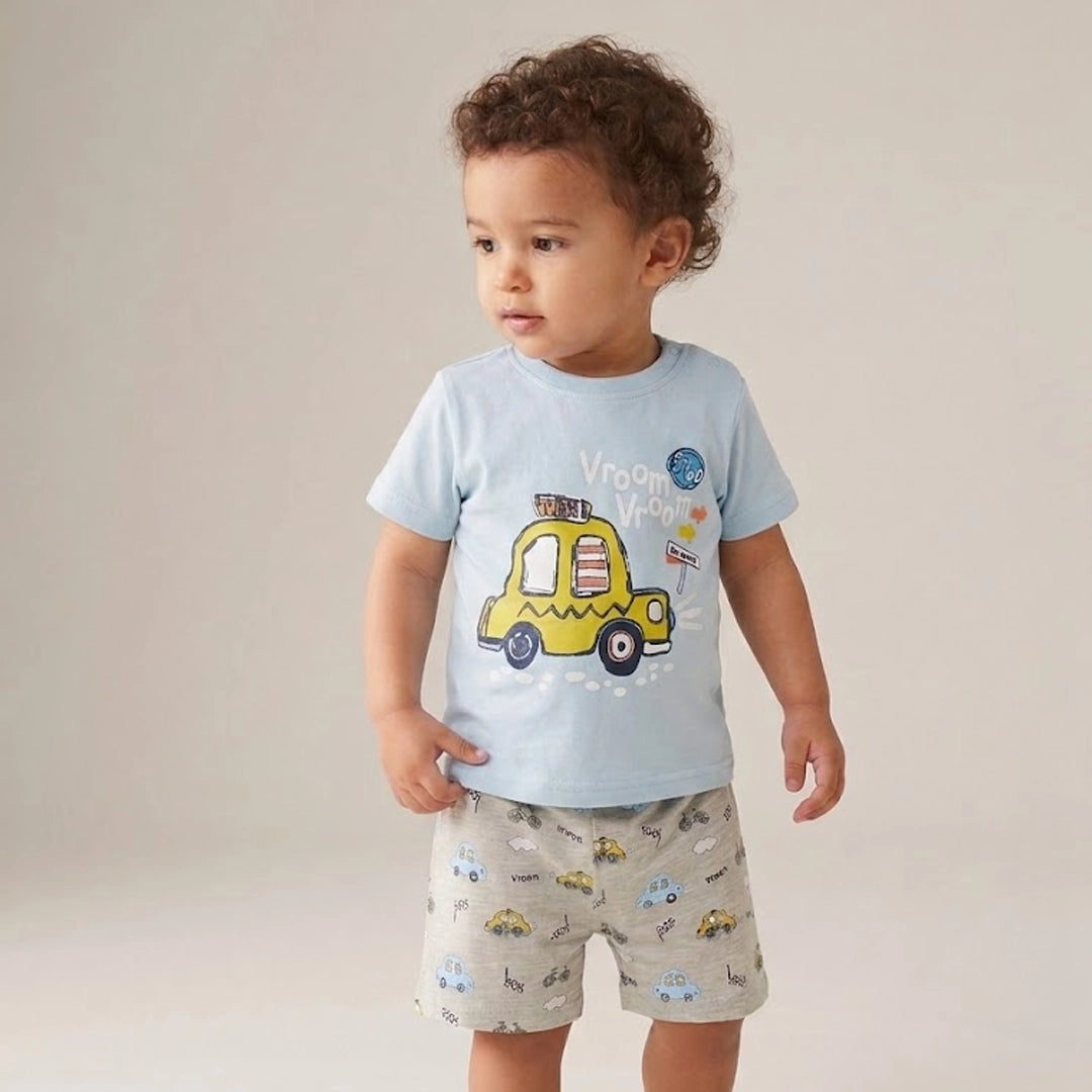 Child wearing a light blue t-shirt with a yellow car design and patterned shorts on a plain background