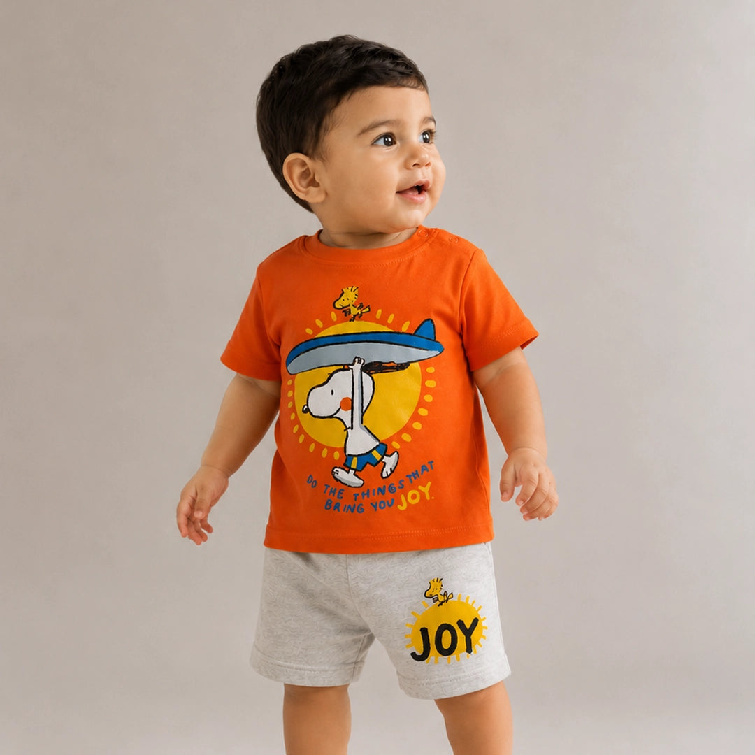 Child wearing an orange t-shirt with a cartoon character and gray shorts on a plain background