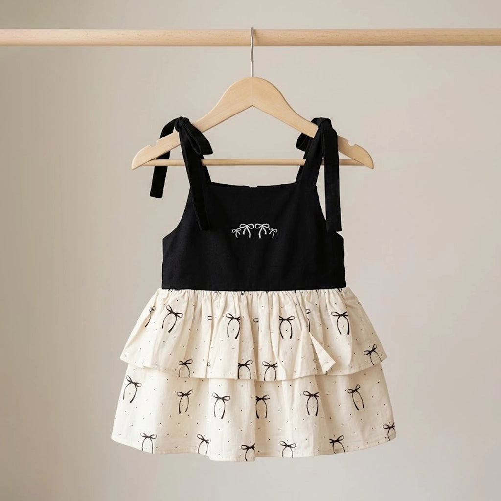 Black top and white skirt with black bow details on a wooden hanger against a beige background