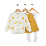 Children's outfit with white cardigan with yellow floral patterns and mustard skirt on hangers against a white background.