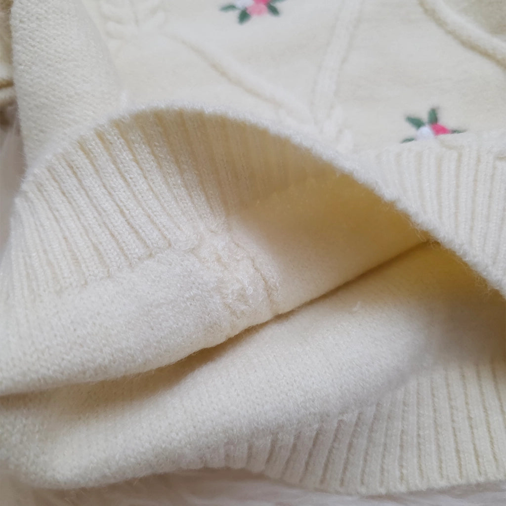 Close-up of a cream-colored sweater with floral embroidery on a soft background