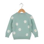 Light green sweater with white daisy patterns on a wooden hanger against a white background
