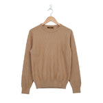 Beige cable knit sweater on a hanger against a white background