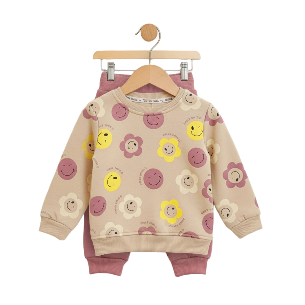 Children's outfit with beige sweatshirt and pink pants featuring smiley face and flower patterns on a white background.