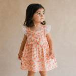 Young girl wearing an orange floral dress against a beige background
