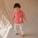 Child wearing a red shirt and colorful pants standing against a beige background