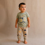 Child wearing a green t-shirt and beige pants with a pattern on a beige background