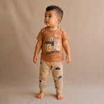 Child wearing a brown t-shirt and patterned pants on a beige background