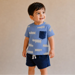 Child wearing a blue t-shirt with animal prints and dark shorts against a beige background