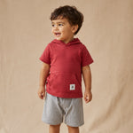 Child wearing a red hoodie and gray shorts on a beige background