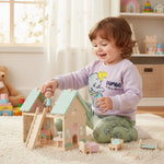 Child playing with a wooden dollhouse in a bright room with toys around