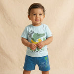 Child wearing a light blue t-shirt with a crocodile and duck design and blue shorts with 'Hello Summer' text on a beige background.