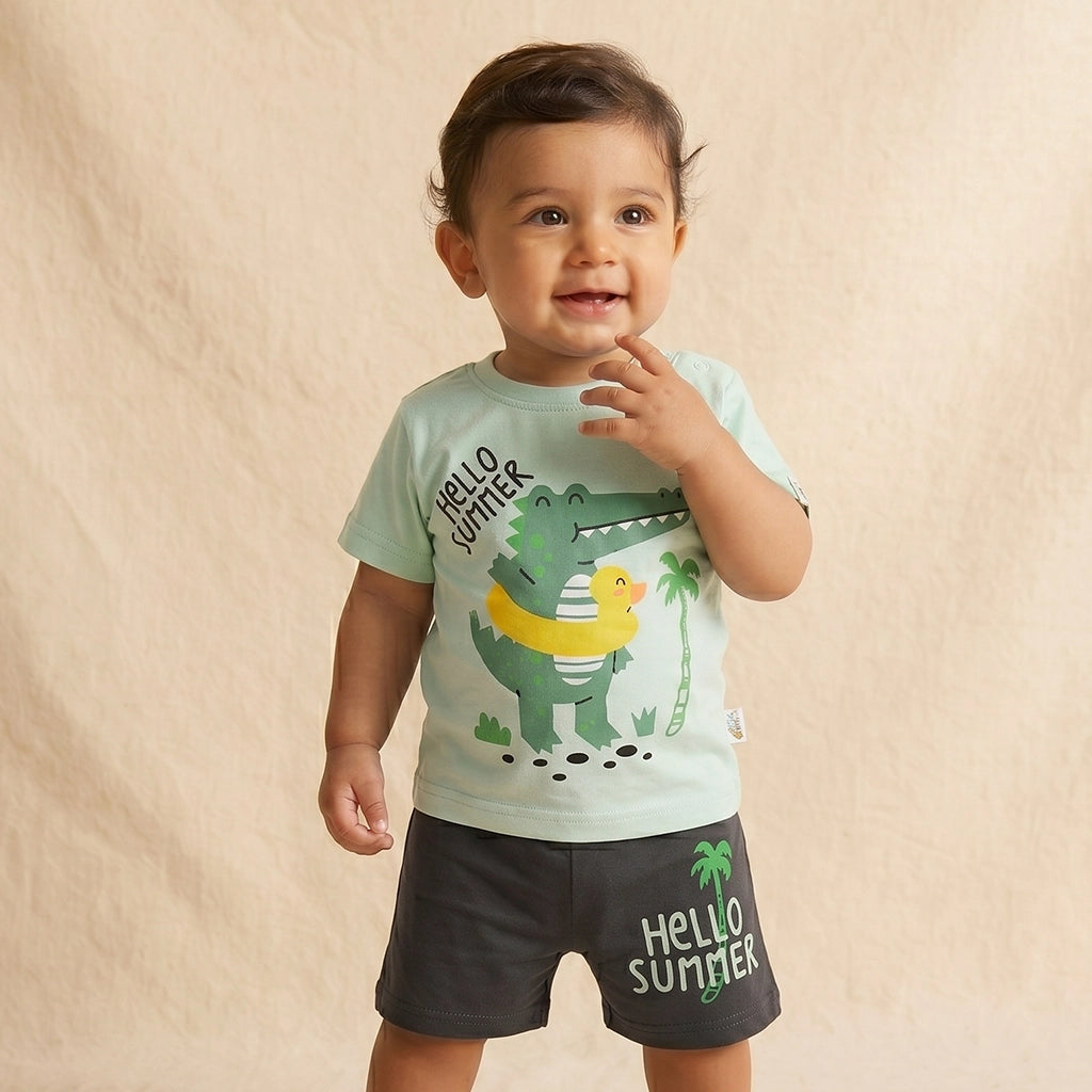 Child wearing a light green t-shirt with a dinosaur and duck design and black shorts with 'Hello Summer' text on a beige background.