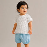 Child wearing a white patterned top and light blue shorts on a plain background