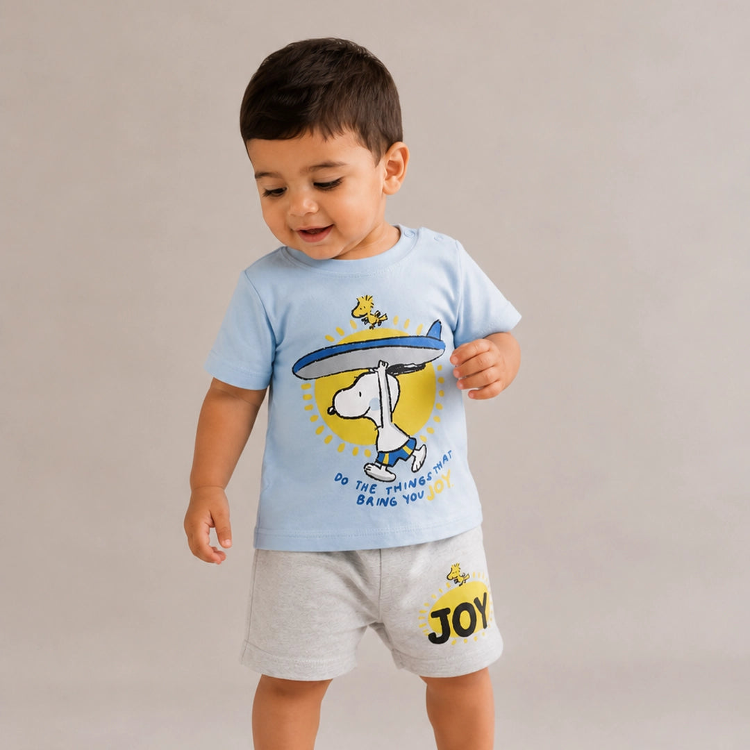 Child wearing a light blue t-shirt with a graphic design and gray shorts with 'JOY' print on a beige background