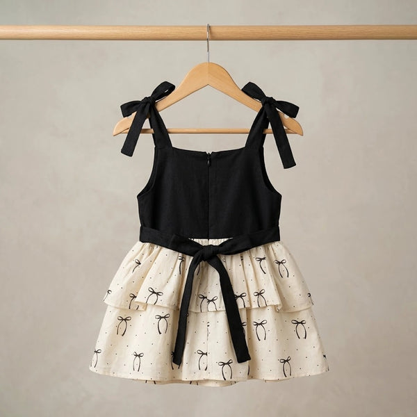 Black top and white skirt with black bow details on a wooden hanger against a beige background
