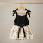 Black top and white skirt with black bow details on a wooden hanger against a beige background