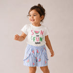 Child wearing a white t-shirt with colorful text and blue striped shorts on a plain background